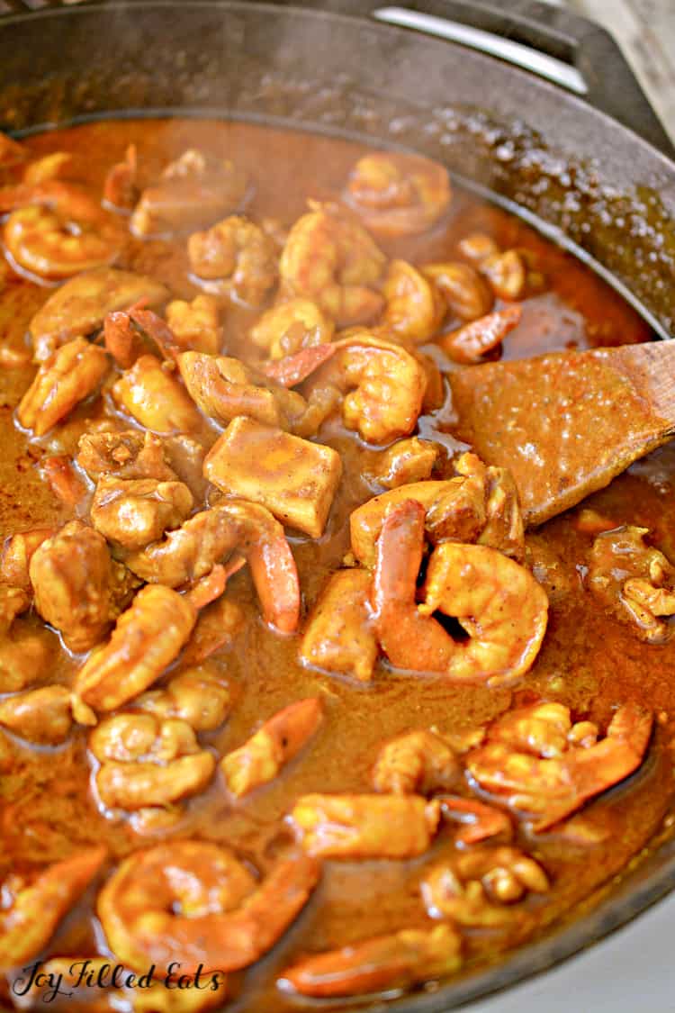 skillet of shrimp curry being mixed with wooden spoon