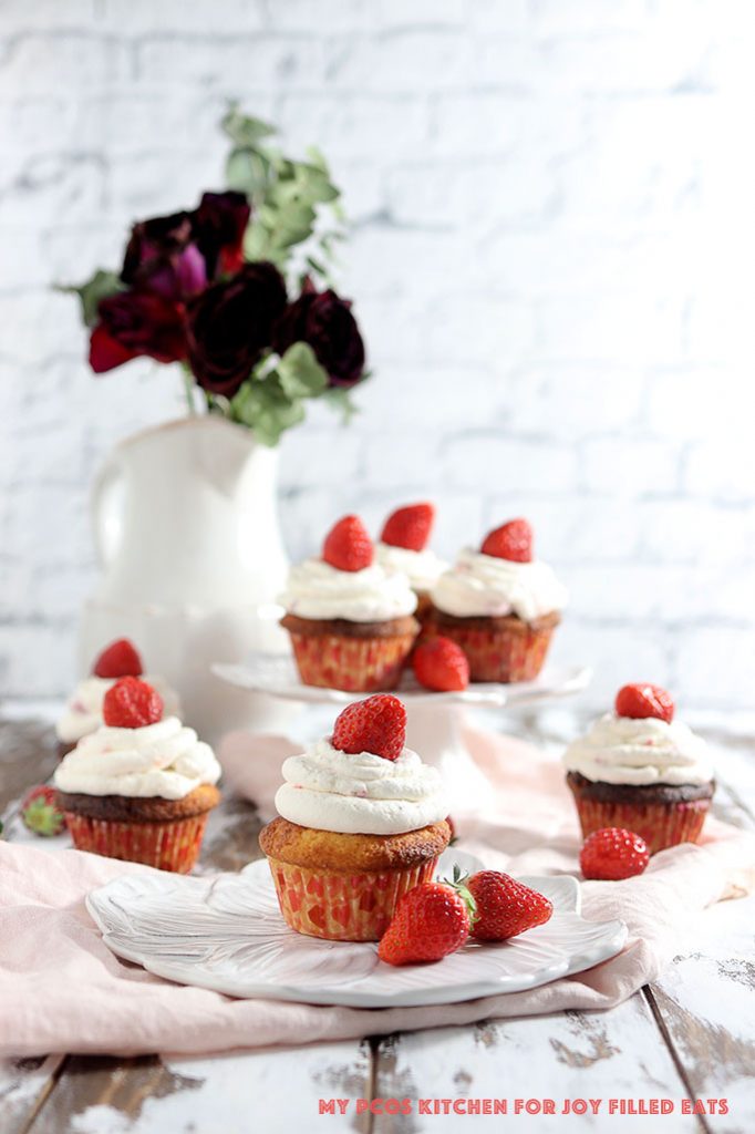 Low carb cupcakes with strawberry whipped cream on different plates with roses in the background.