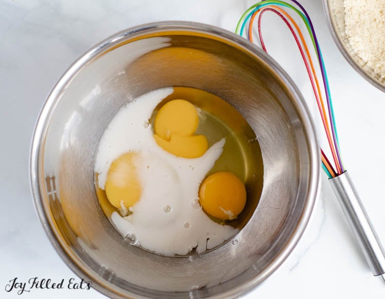 wet ingredients and eggs combined in a mixing bowl next to a whisk for pancake batter