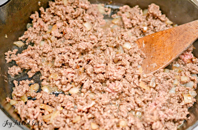 ground beef being cooked in a skillet with a wooden spoon