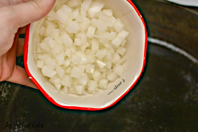 hand holding chopped onions in mall bowl to be added to skillet