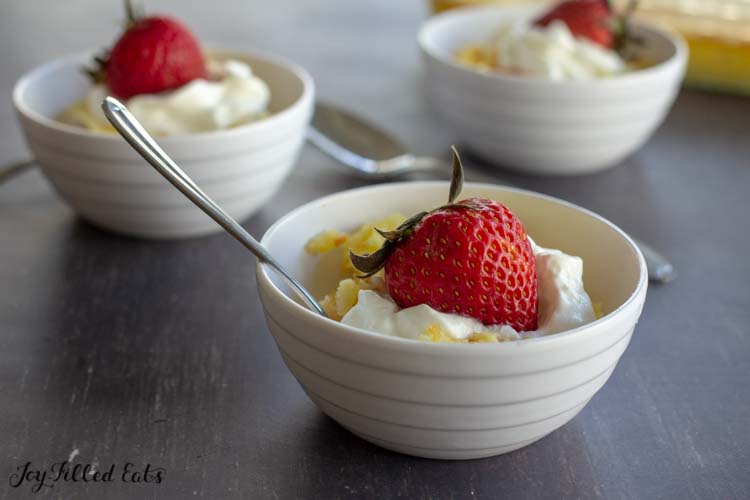 Bowls of baked custard with lemon topped with whipped cream and a whole strawberry