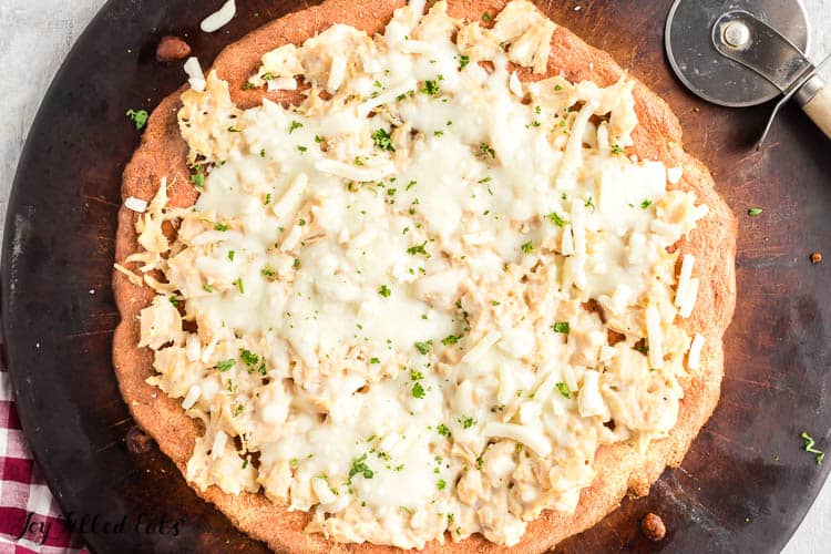 chicken Alfredo pizza placed on round pizza stone with pizza cutter up close