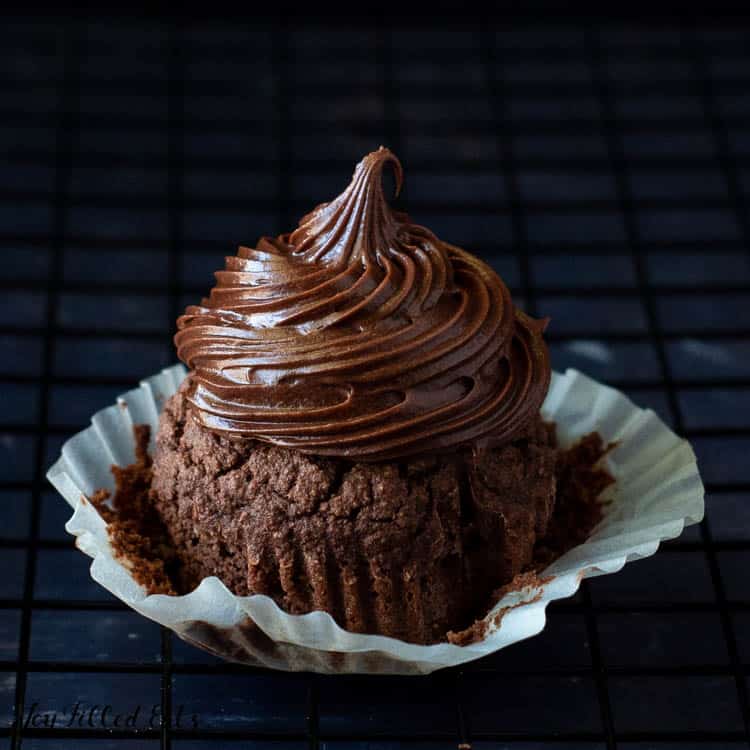 chocolate cream cheese iced chocolate cupcake with cupcake wrapper pulled back on a cooling rack close up