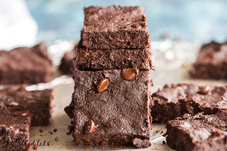 stack of flourless fudge brownies with one brownie leaning on stack surrounded by more fudge brownies