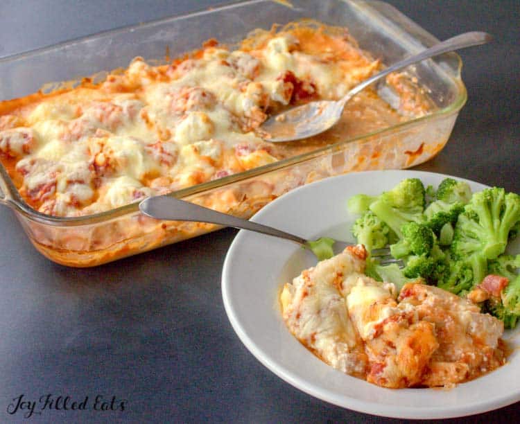 plate of chicken pizza casserole and broccoli with fork next to casserole dish of remaining chicken pizza casserole with serving spoon