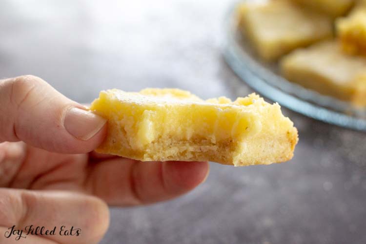 hand holding lemon square with bite taken out of corner