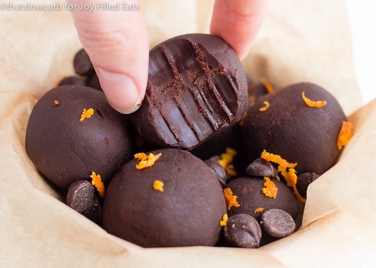 hand placing orange fudge fat bomb with bite marks into bowl of more fat bombs and chocolate chips