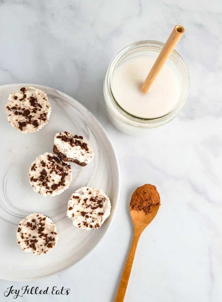 plate of oreo cheesecake bites next to a glass of milk and paper straw and small wooden spoon