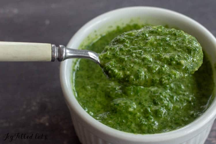 spoon holding a scoop of pesto sauce from small dish below