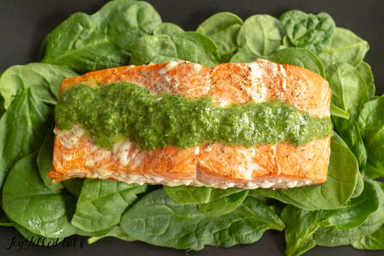 plate of baby spinach topped with a salmon filet and drizzled in a line of pesto sauce