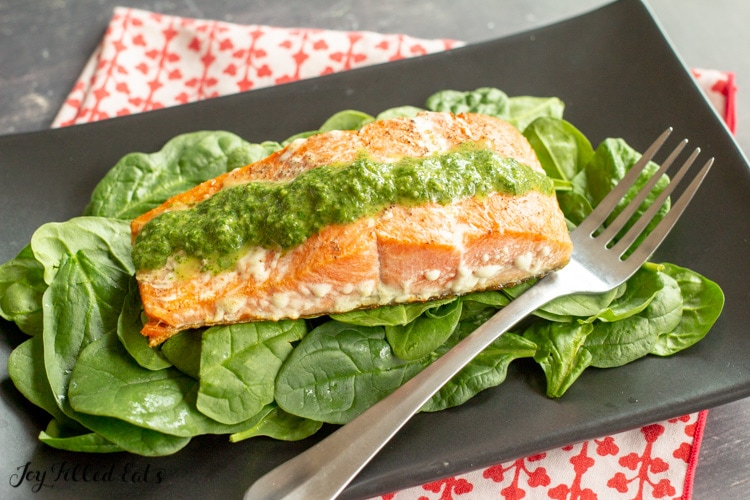 a black plate with salmon from the pesto salmon recipe on top of a bed of baby spinach