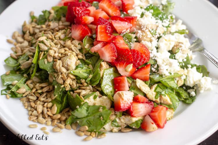 baby spinach salad topped with diced strawberries, feta cheese and sunflower seeds in a shallow bowl with fork