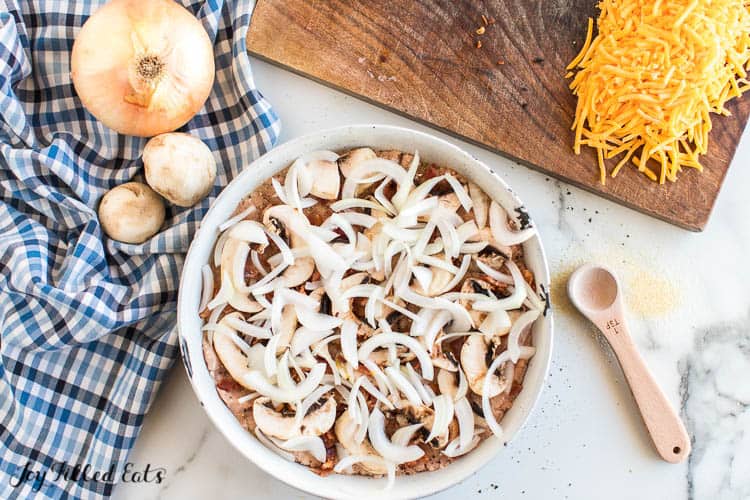 burger bake casserole dish topped with sliced onion before baking
