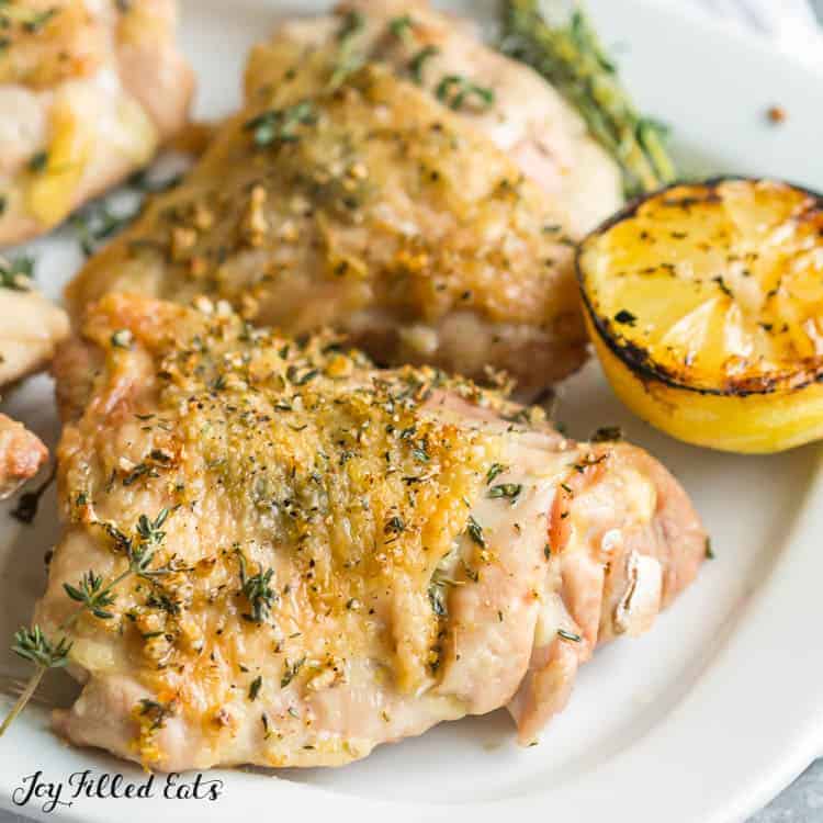 lemon garlic baked chicken thighs on a plate with a charred half a lemon close up