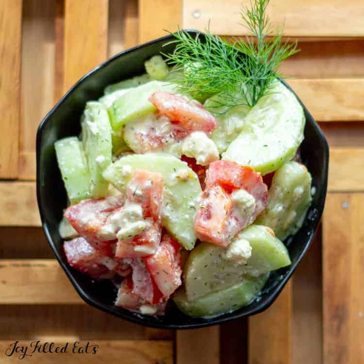 cucumber and tomato salad garnished with fresh dill in black bowl from above