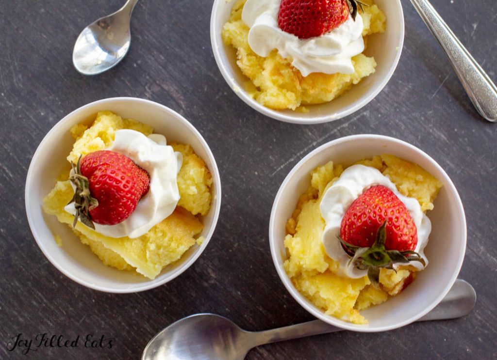 servings of baked custard in small white bowls with spoons topped with whipped cream and a strawberry from above