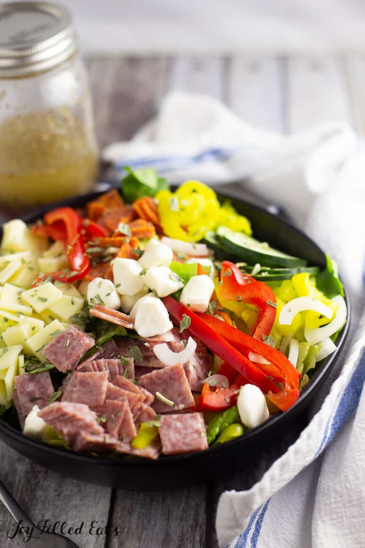 Italian sub salad in a black bowl next to a jar of dressing close up