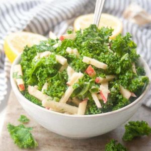 kale salad with matchstick sliced apples in white bowl