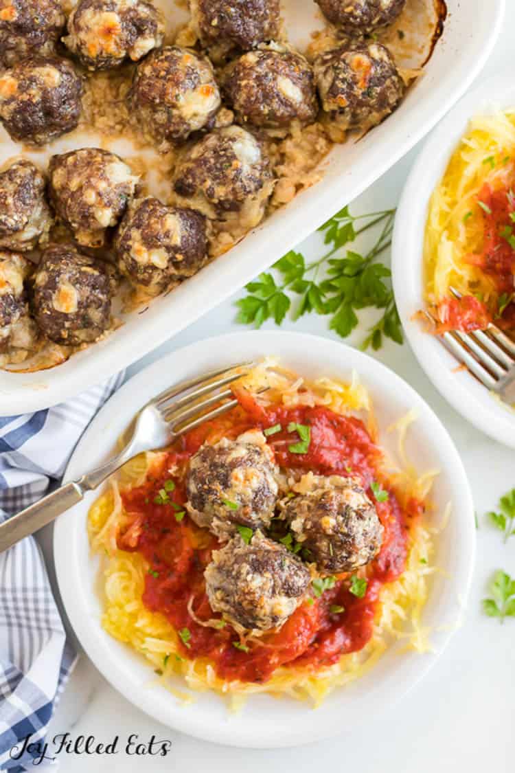 keto meatballs on top of a plate of spaghetti squash and sauce with fork set next to a casserole dish filled with more keto meatballs from above