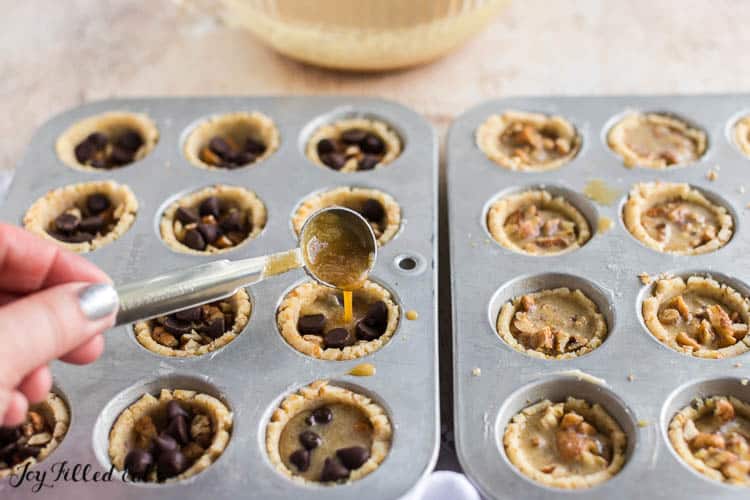 hand pouring tassie mixture into muffin tin of chocolate chip tassies set next to muffin tin of pecan filled tassies