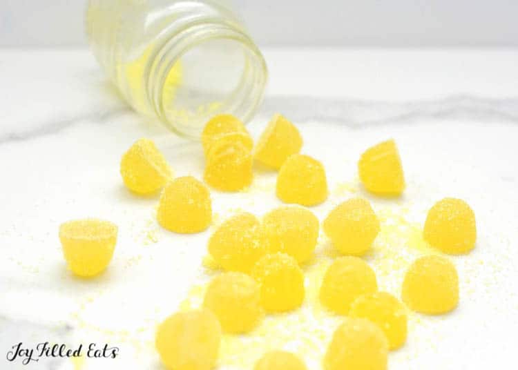 sour lemon gumdrops spilling out of mason jar on white table surface