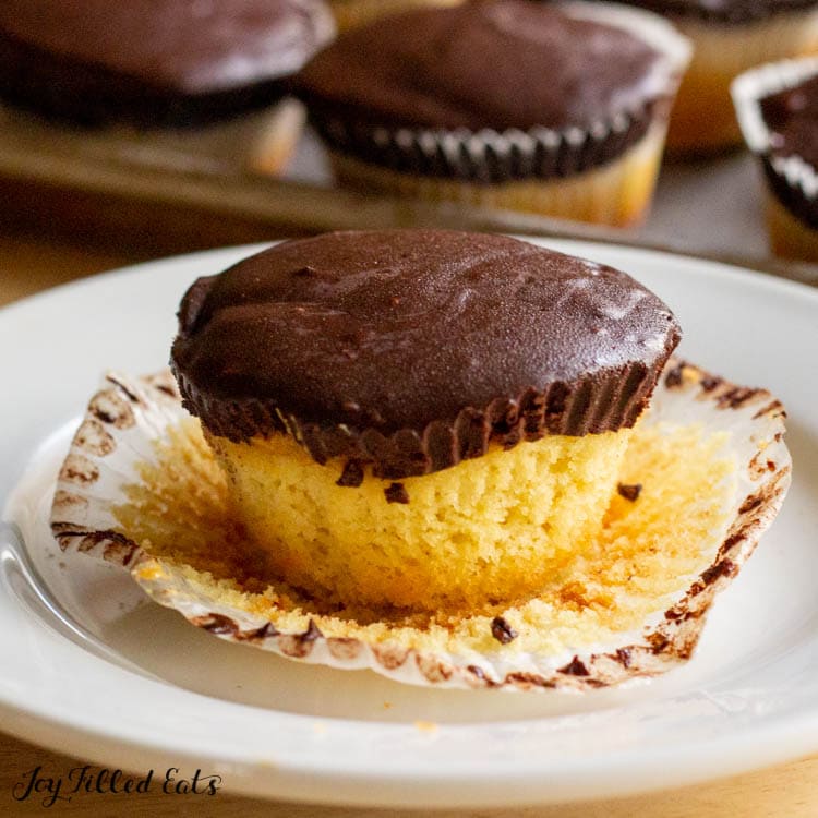 vanilla cupcake filled with peanut butter and topped with chocolate ganache on a white plate