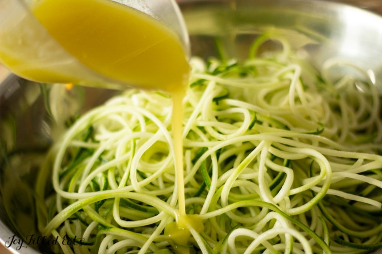 close up shot of pouring the lemon dressing over the zucchini noodles