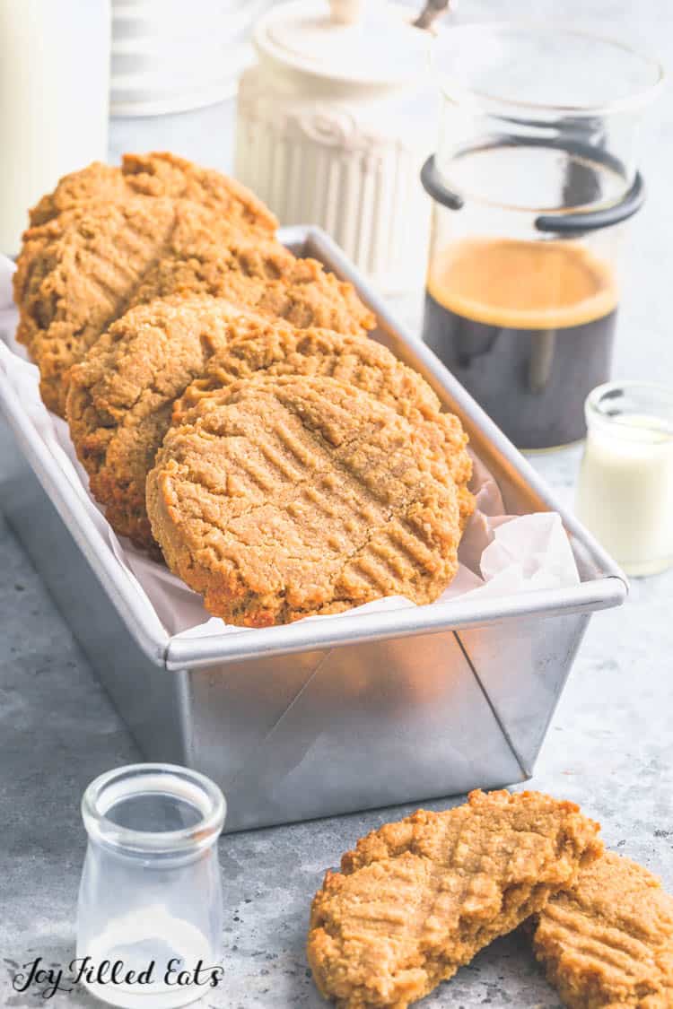 Flourless Peanut Butter Cookies placed in a parchment lined bread pan set next to two halves of a cookie on surface