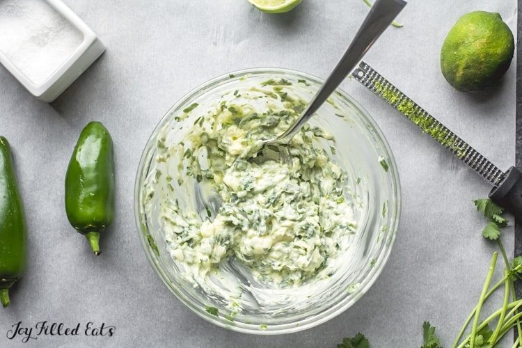 bowl of cilantro-lime butter surrounded by jalapeno peppers, limes and a zester