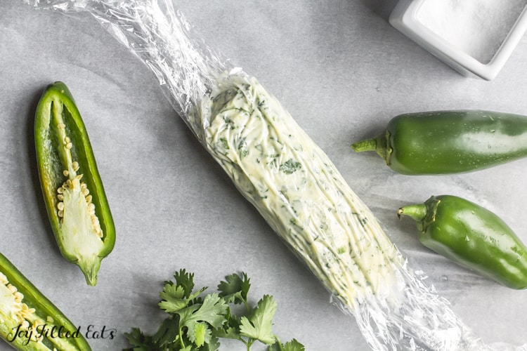 cellophane wrapped cilantro-lime butter placed next to whole and halved jalapeno peppers