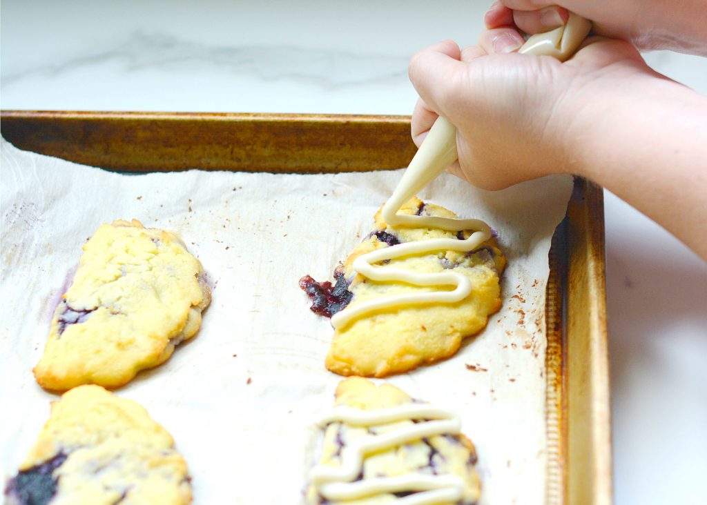 hand piping icing onto blueberry turnovers on a parchment lined sheet pan