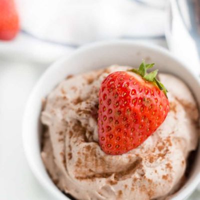 Keto Chocolate Mousse in small white bowl topped with a whole strawberry and sprinkled in cocoa powder close up