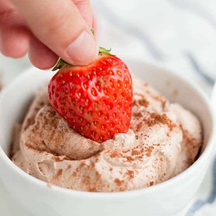 a hand dipping a strawberry into the Keto Chocolate Mousse