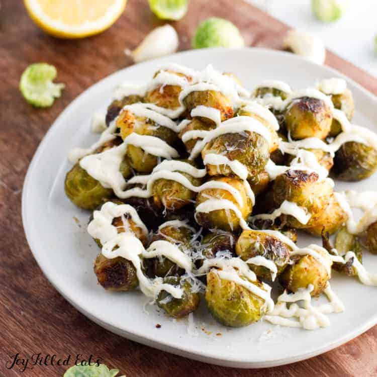 grilled Brussels sprouts on a white plate drizzled in lemon aioli set on a cutting board close up