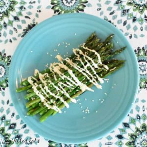 grilled asparagus drizzled in sauce and sesame seeds on a blue plate set on a decorative table cloth