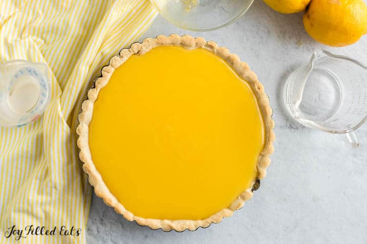 overhead view of plain lemon curd tart surrounded by measuring cups and lemons