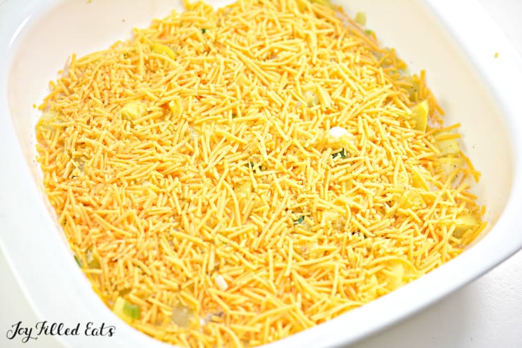 casserole dish of yellow squash casserole before baking topped with shredded cheese