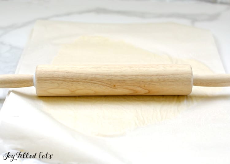 rolling pin on top of parchment paper with turnover dough beneath