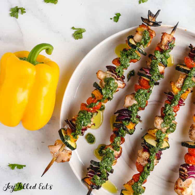 chimichurri chicken kebabs on a plate next to a yellow bell pepper from above