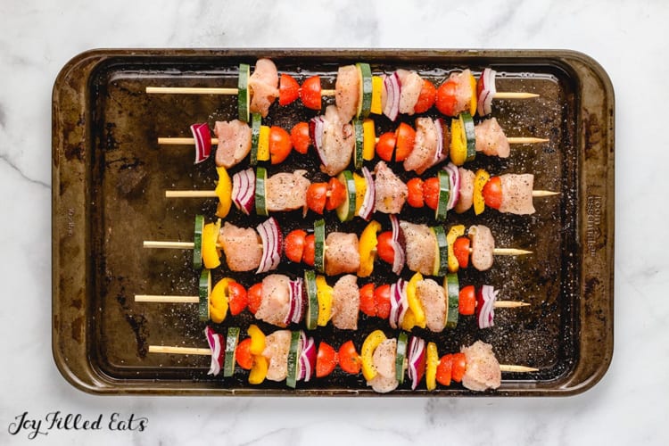 chicken skewers lined on a sheet pan before cooking