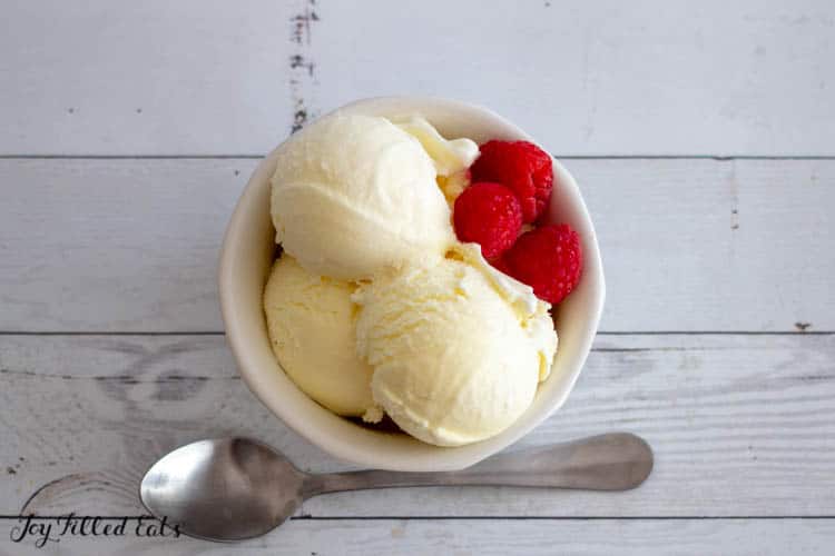 frozen custard scoops with raspberries in small white dish next to a spoon from above