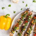 chimichurri chicken kebabs on a plate next to a yellow bell pepper and garlic bulb from above