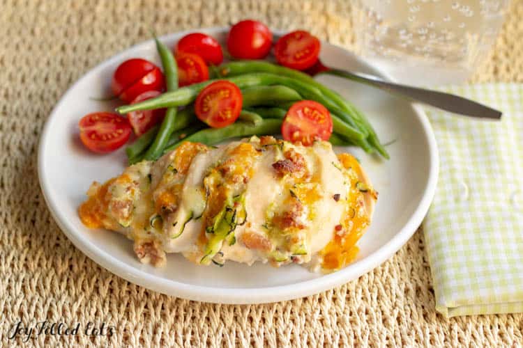 Four Cheese Bacon Hasselback Chicken on a wide plate with green beans and tomatoes