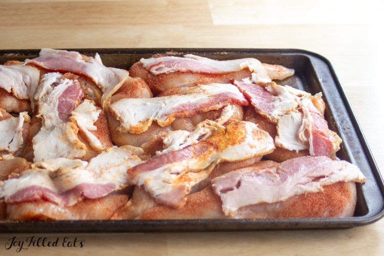 sheet pan full of bacon strips placed on chicken pieces 