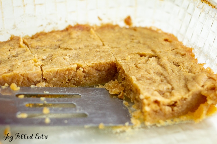 serving spatula in a baking dish lined with pre-cut white chocolate keto peanut butter blondies