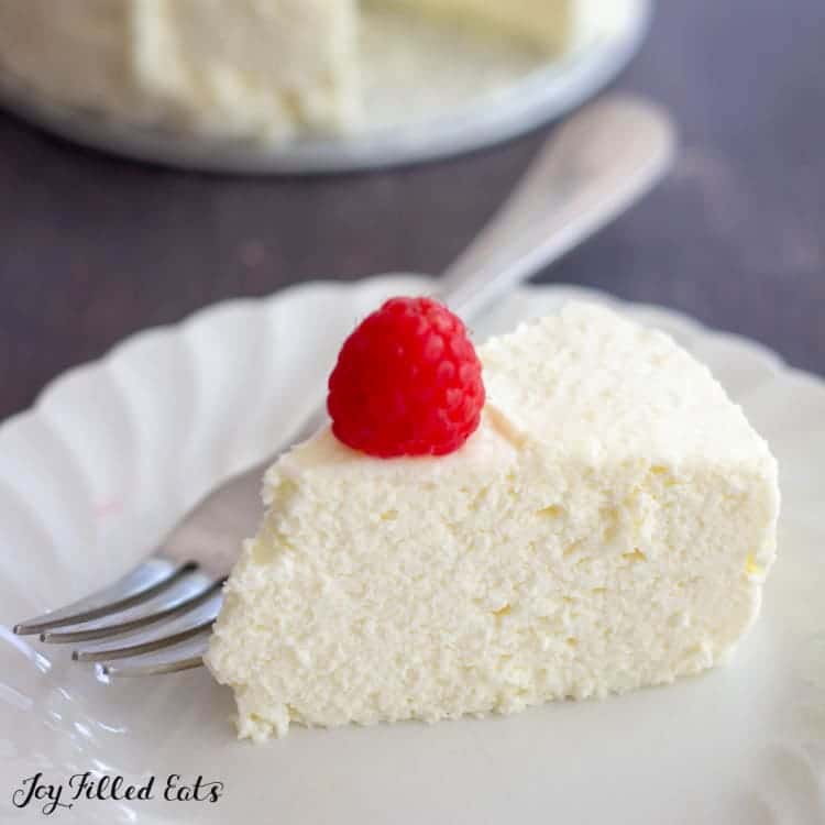 slice of mascarpone cheesecake on a white plate with a fork and topped with one raspberry close up