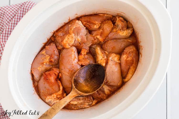chicken pieces and seasoning from above in crockpot with a wooden spoon