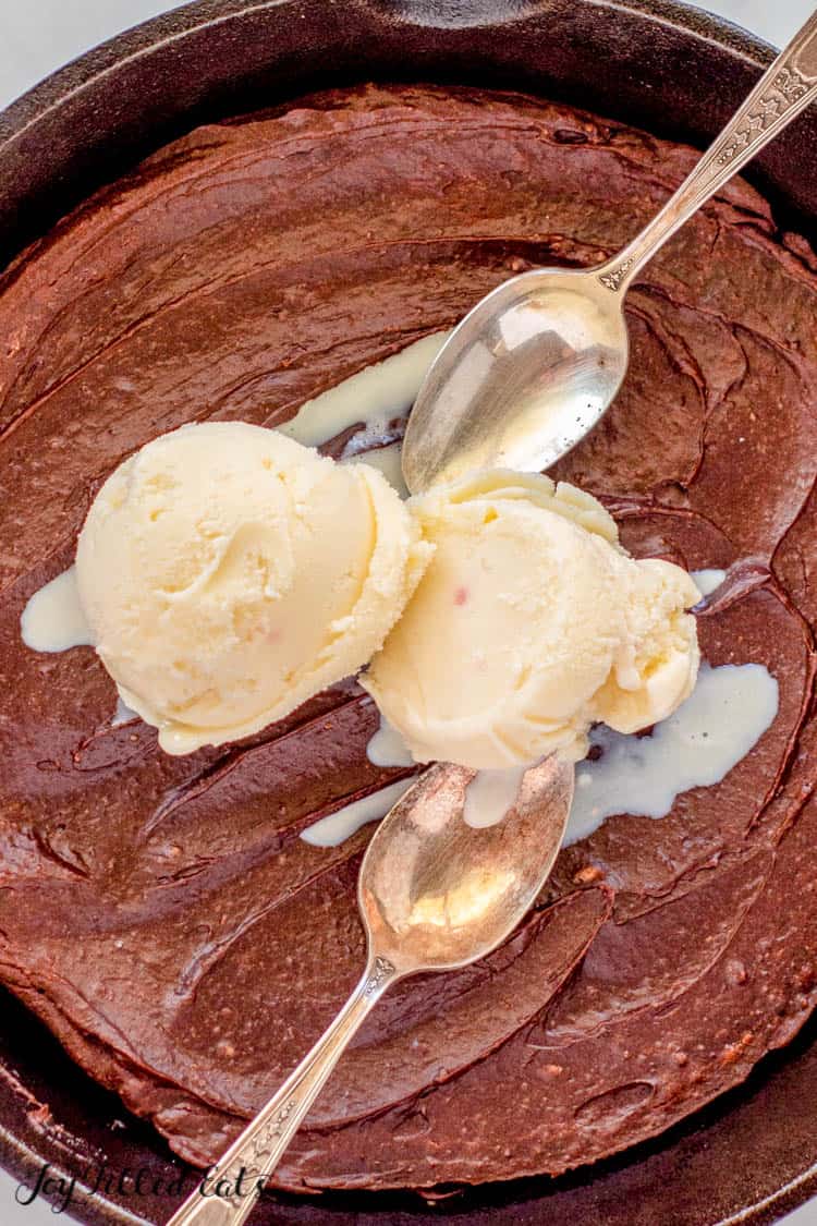 close up of gluten-free peanut butter brownies in skillet with two scoops of ice cream and two spoons