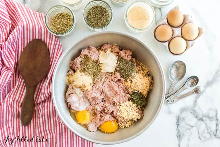 large mixing bowl of meatloaf ingredients surrounded by a wooden spoon, eggs and more seasonings